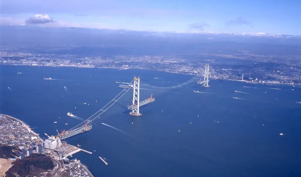 Aerial view of the Akashi Kaikyo Bridge under construction in December 1995, both towers standing with the main cables strung and the deck not yet erected