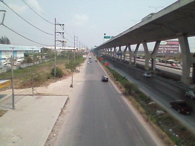 The elevated concrete deck of the Bang Na Expressway on single piers, running alongside a ground-level highway in Thailand