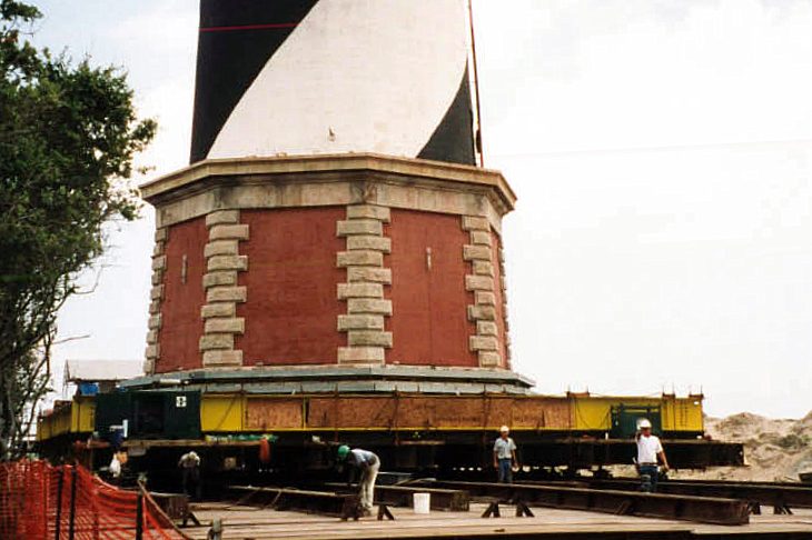 The base of the Cape Hatteras Lighthouse resting on its steel support frame and roller track, with workers preparing the next increment of movement