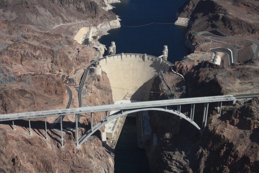 Aerial view of Hoover Dam in Black Canyon with Lake Mead behind it, the intake towers on the upstream side, the power plant at the foot of the dam and the highway bypass bridge crossing the canyon in front
