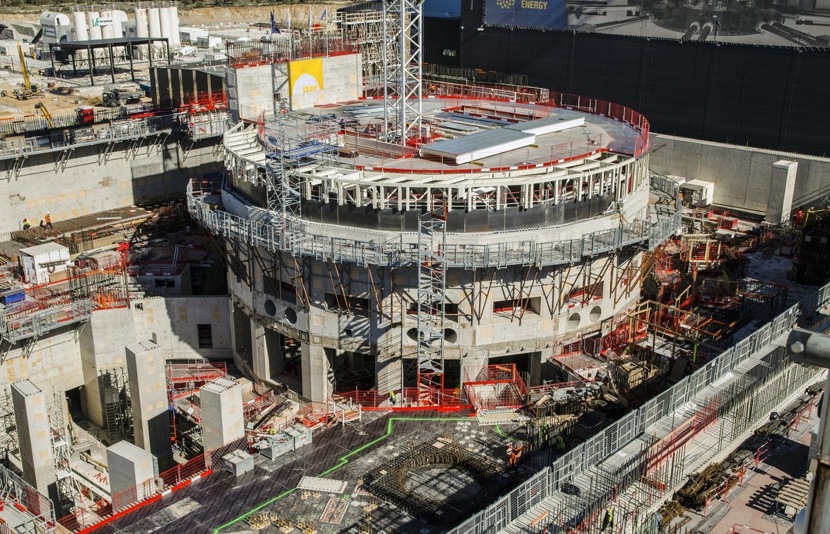 The circular ITER Tokamak Complex under construction, surrounded by scaffolding, safety railings and concrete walls