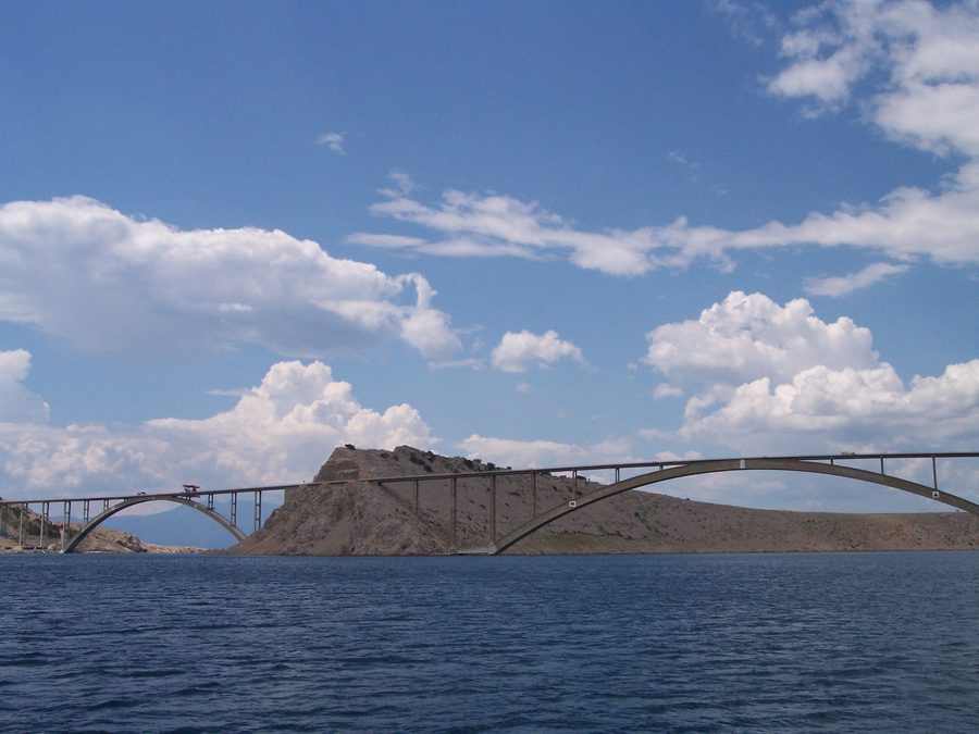 The Krk Bridge seen from the sea: the smaller and larger concrete arches either side of the rocky islet of Sveti Marko, with the deck carried on slender columns above each arch