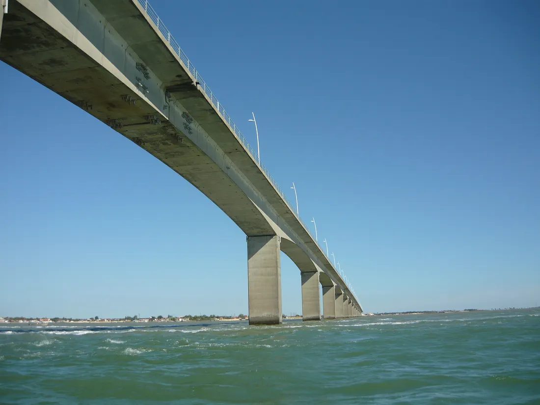 The Oleron Viaduct's precast box-girder deck seen from below and behind, carried on a line of tapered concrete piers across the Coureau d'Oleron