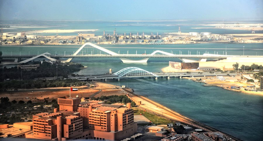 Aerial view over Abu Dhabi looking across the Maqta Channel toward the Sheikh Zayed Bridge and Maqta Bridge, with an industrial facility on the far shore, 2013