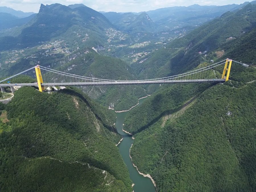 Aerial view of the Sidu River Bridge, a suspension bridge with two yellow towers carrying a single deck across a deep, forested gorge in western Hubei, China.