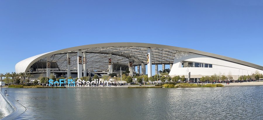 SoFi Stadium's translucent ETFE canopy roof viewed from ground level beside the lake at its entrance plaza, Inglewood, California