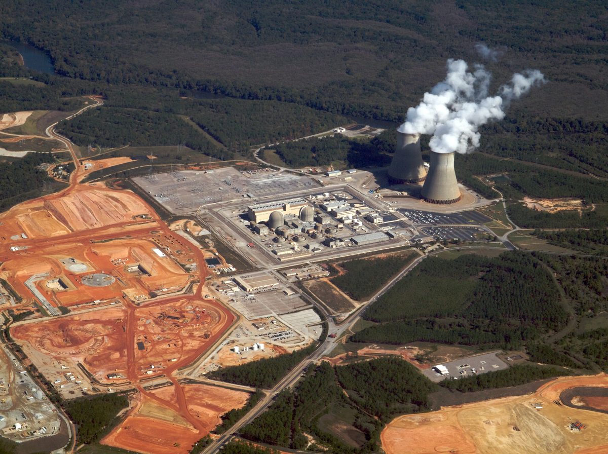 Aerial view of the Vogtle site: the existing domed Units 1 and 2 and their cooling towers in the centre and right, with the cleared construction site for Units 3 and 4 in red earth on the left