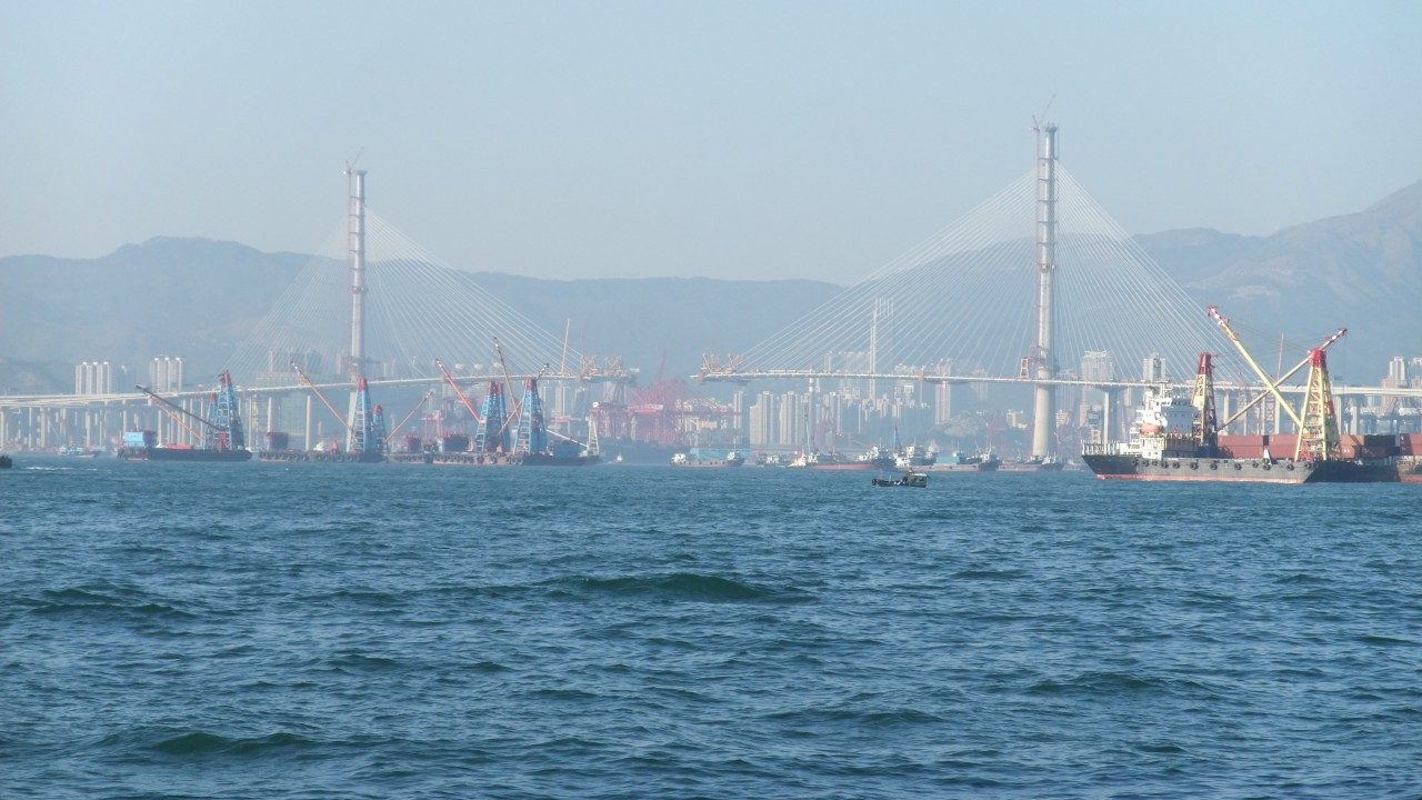 Stonecutters Bridge under construction in Hong Kong, its two towers carrying fanned stay cables above the partially completed deck, with floating cranes working below