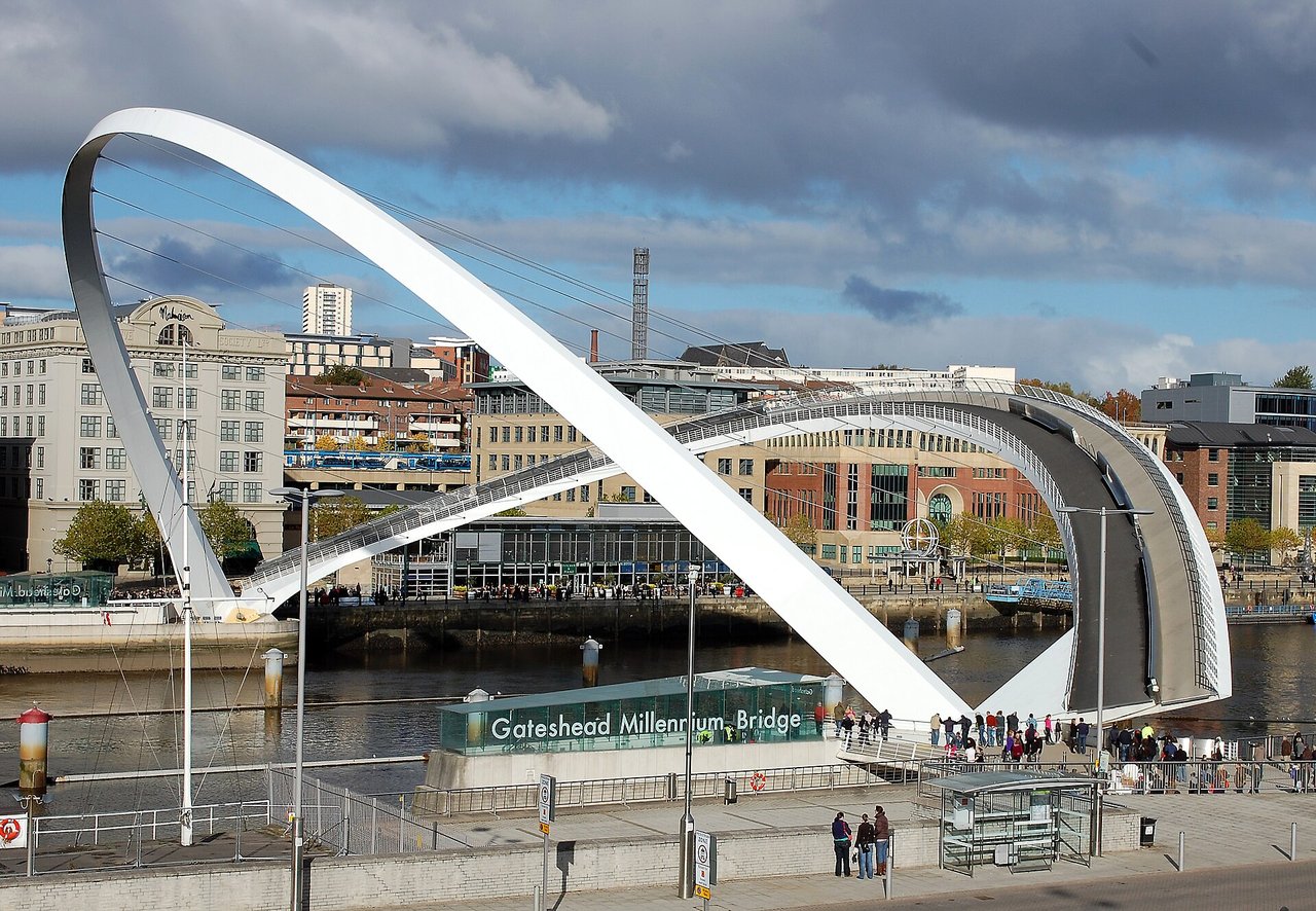 The Gateshead Millennium Bridge on the River Tyne, tilted open, its deck arch raised and supporting arch lowered, with Newcastle Quayside behind