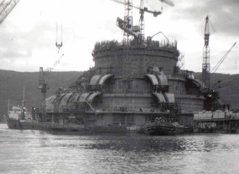 The Ninian Central concrete gravity platform nearing completion in a Scottish construction basin, surrounded by tower cranes and a support vessel