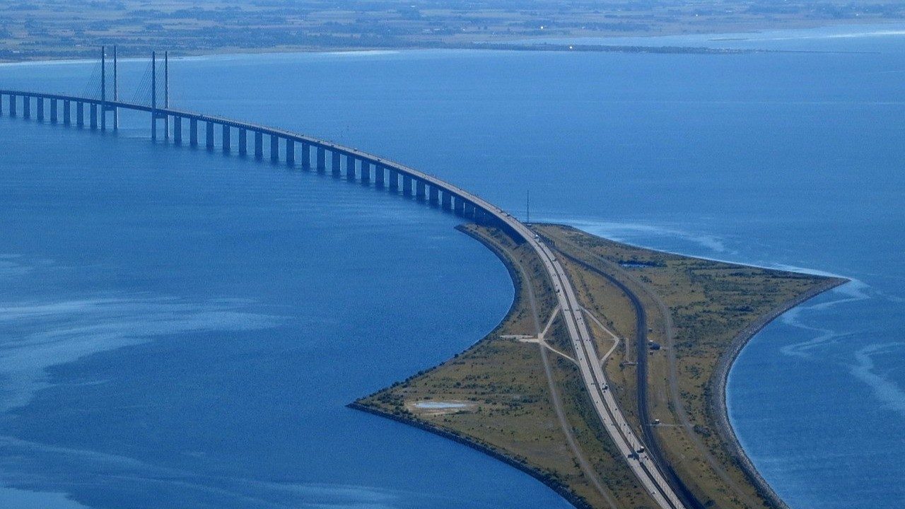 Aerial view of the Øresund Bridge cable-stayed span curving onto Peberholm, the artificial island where the bridge transitions to the immersed tunnel